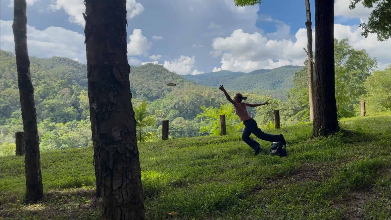 A player driving a disc across a grassy fairway with the Doi Saket mountains behind at Rock n' River